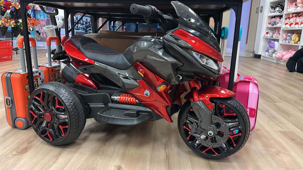A glossy red three-wheeled ride-on motorbike for kids