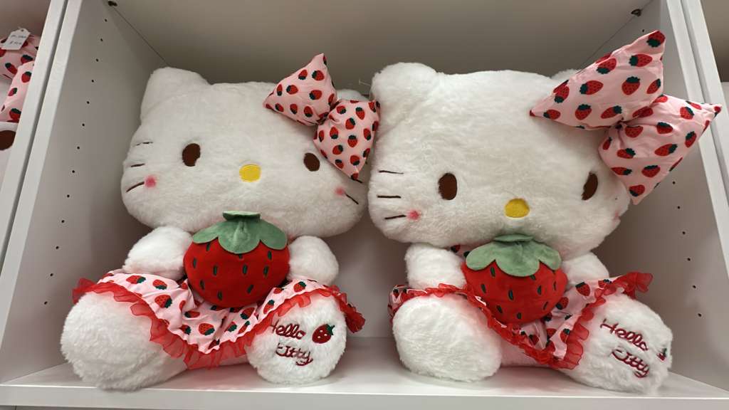 Two fluffy strawberry-themed Hello Kitty plush toys on a shelf
